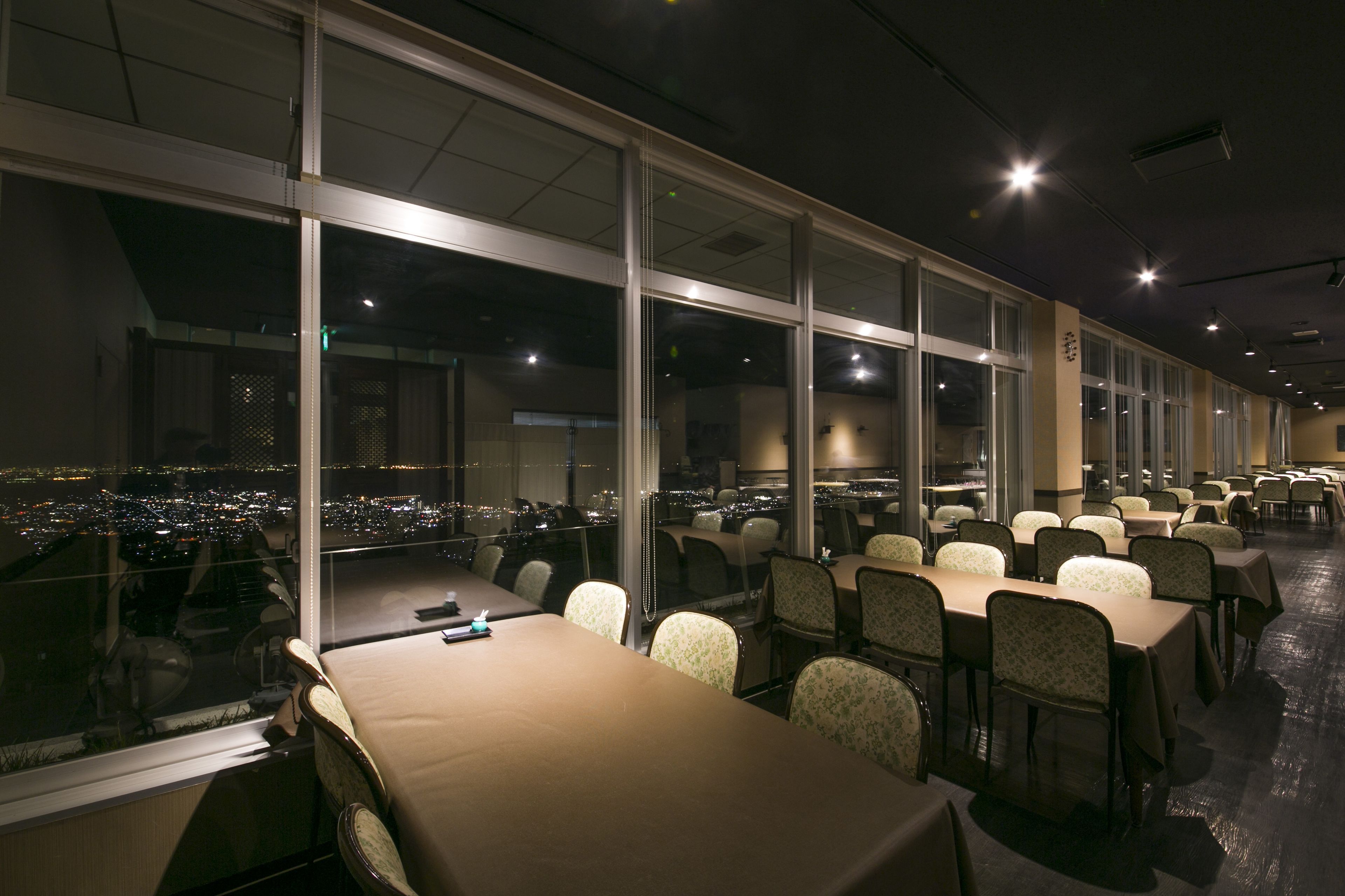 A conference room with tables and chairs, large windows, and city lights visible outside.