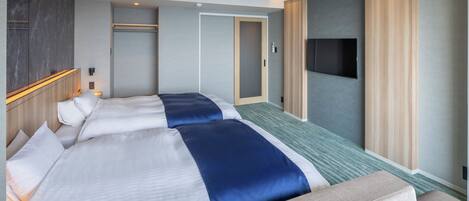 A hotel room with two beds, a sofa, a TV, and a wardrobe.