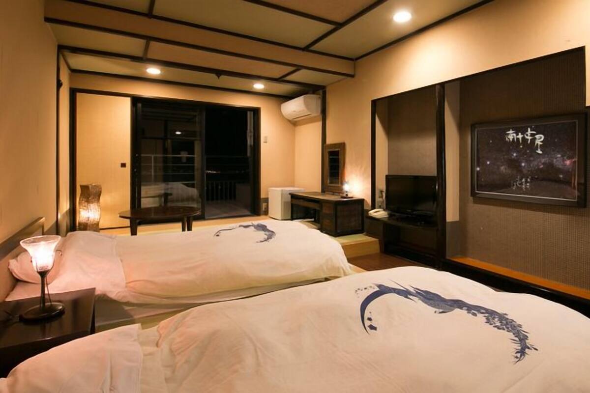 A hotel room with two beds, a desk, a chair, a TV, and a balcony.