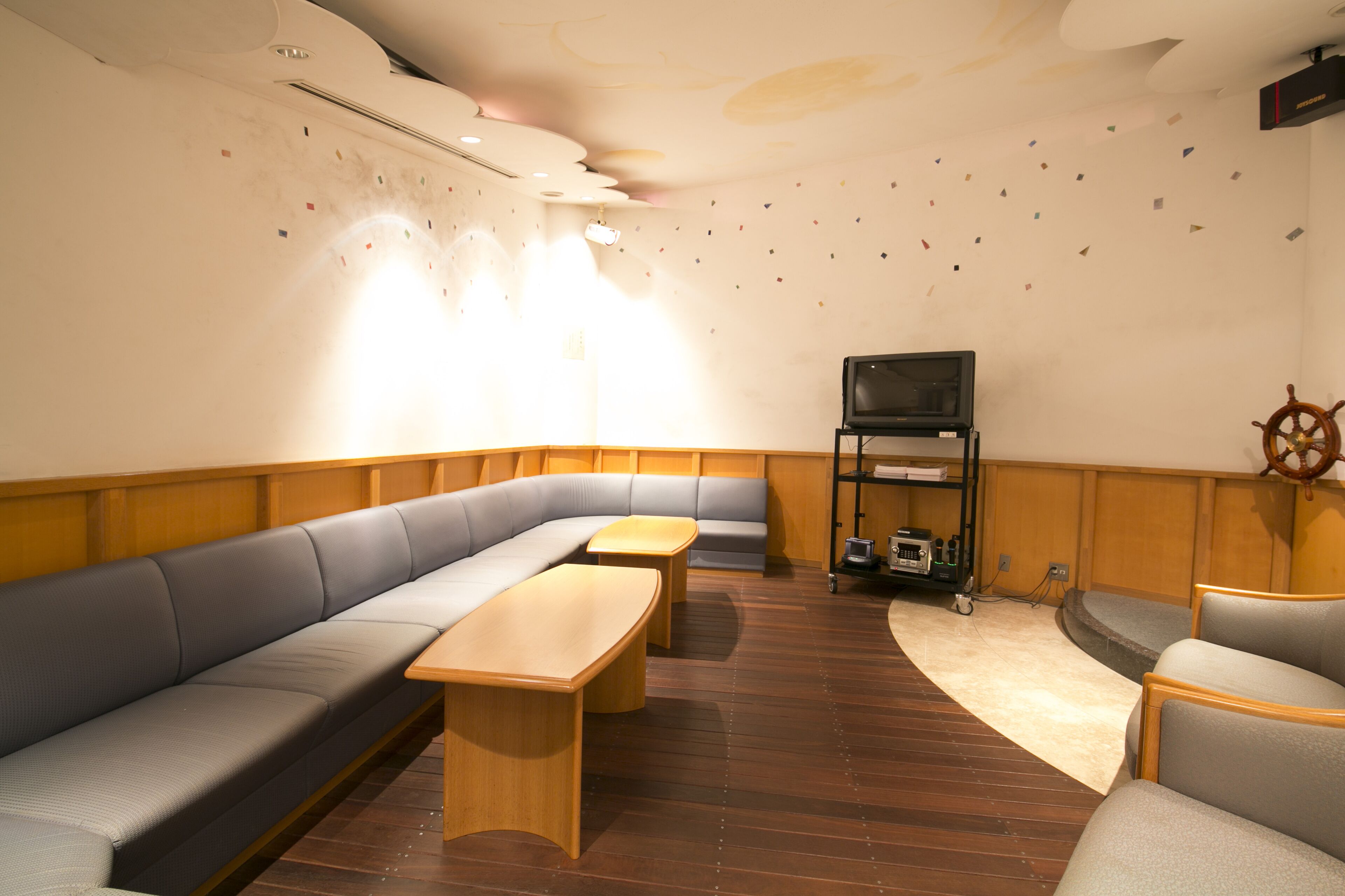 A cozy room with a curved wooden floor, a grey sofa, a wooden table, and a television on a stand.
