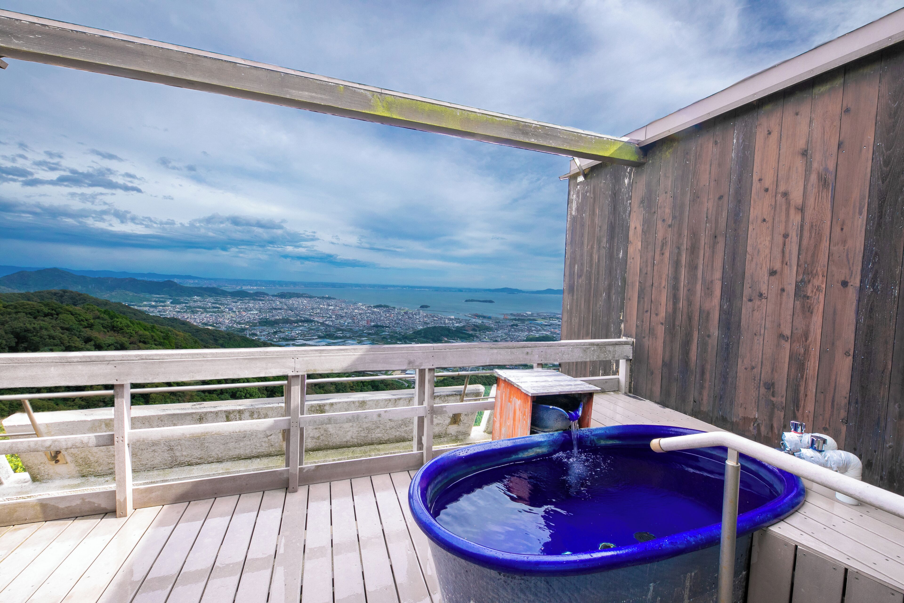 Une terrasse en bois avec un jacuzzi et une vue sur la ville et les montagnes.