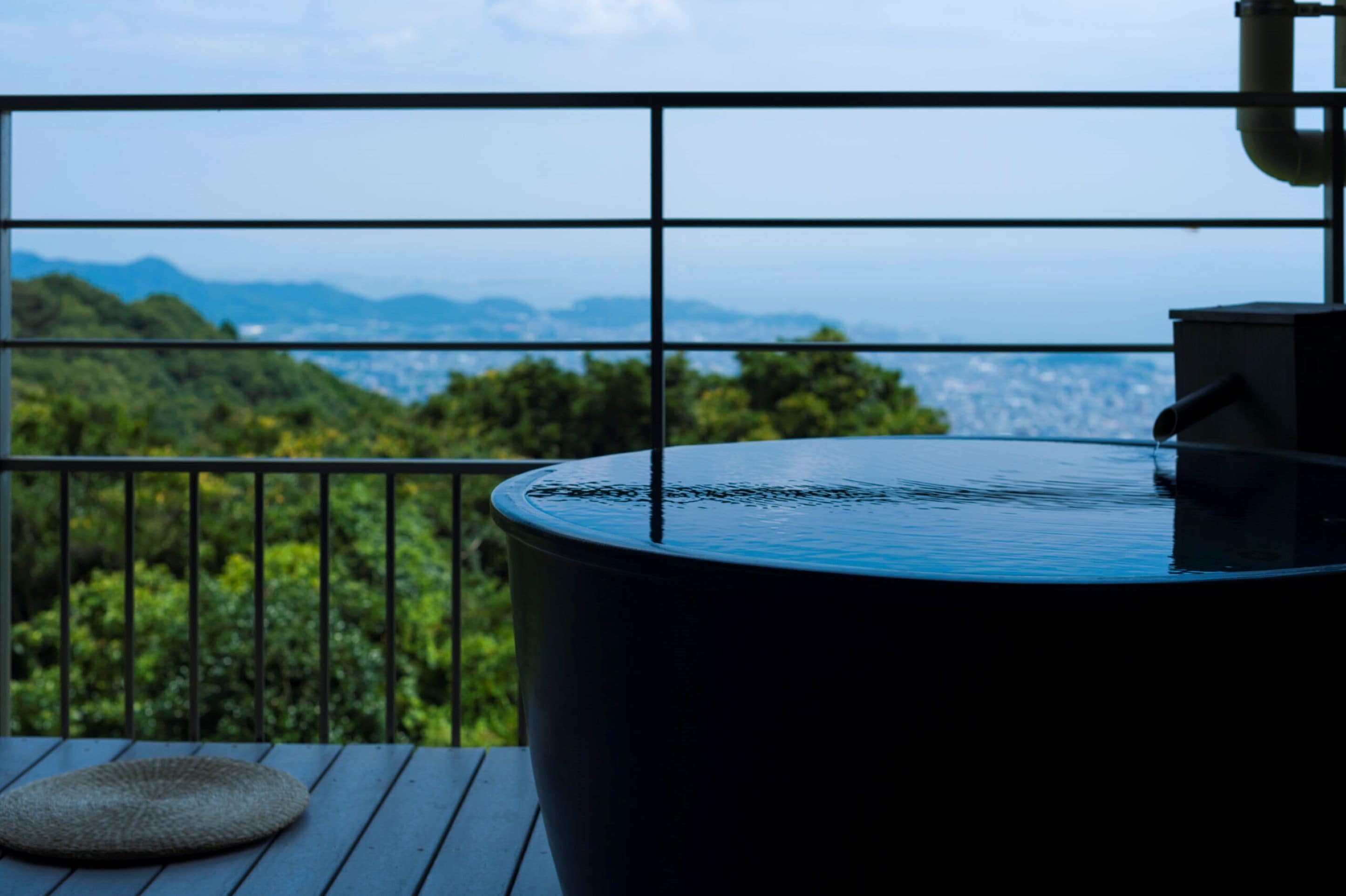 A balcony with a hot tub, a woven mat, and a view of a mountainous landscape.
