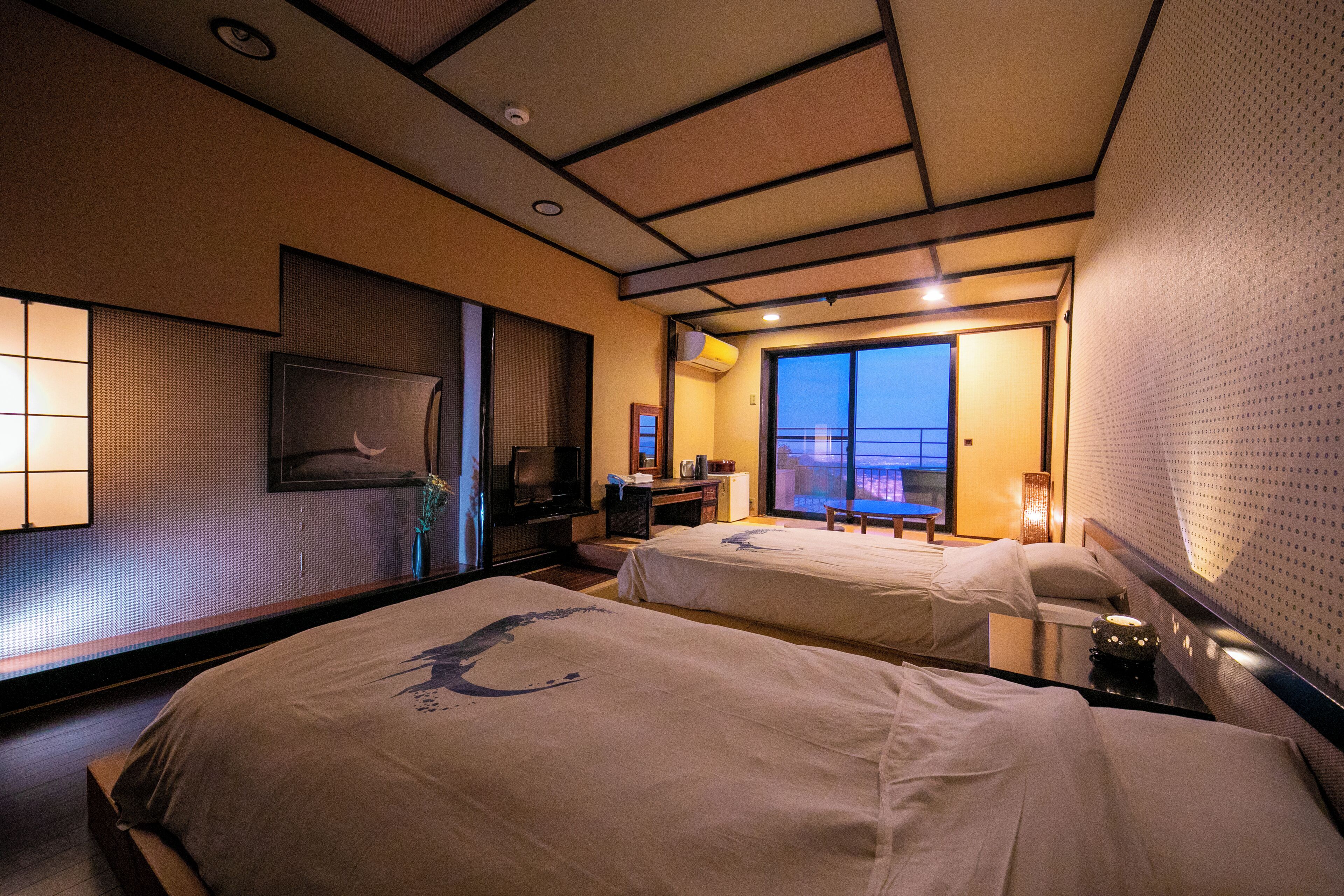 Een hotelkamer met twee bedden, een televisie, een bureau en uitzicht op zee.