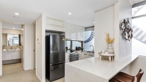 A modern kitchen with a marble countertop, stainless steel appliances, and a view to the living area. - Nautica Residences Fremantle (East Fremantle)