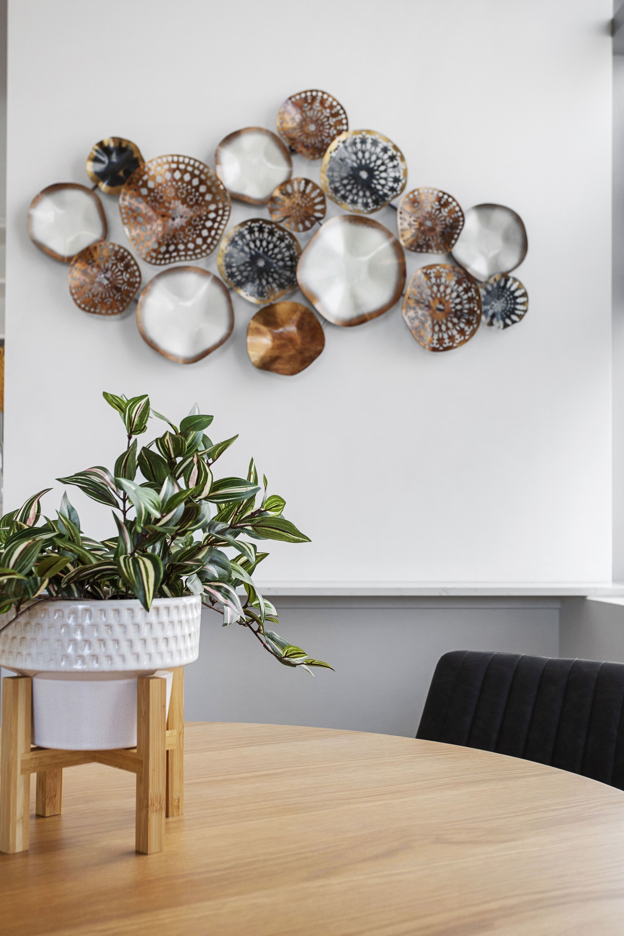 A dining area with a round wooden table, a white textured pot with a plant, and a wall decorated with circular patterned wall art.