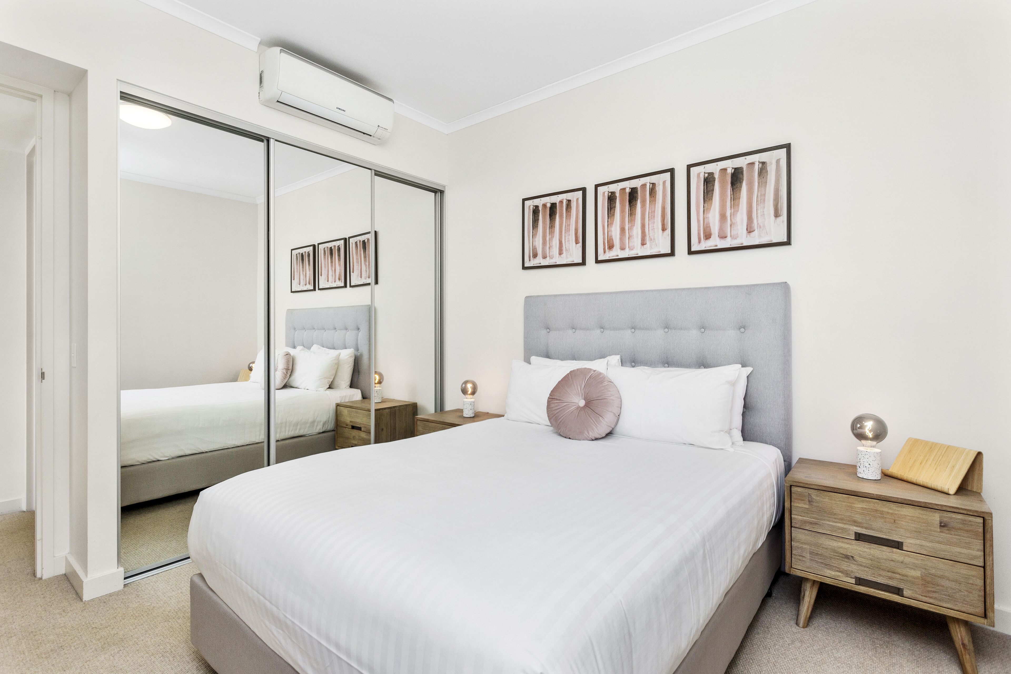 A bedroom with a large bed, a wardrobe with a mirror, bedside tables, and framed artwork on the wall.