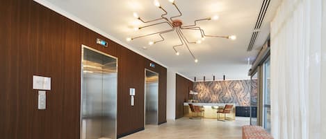 A modern lobby with a wooden wall, elevators, a patterned wall, a reception desk, and a bench.