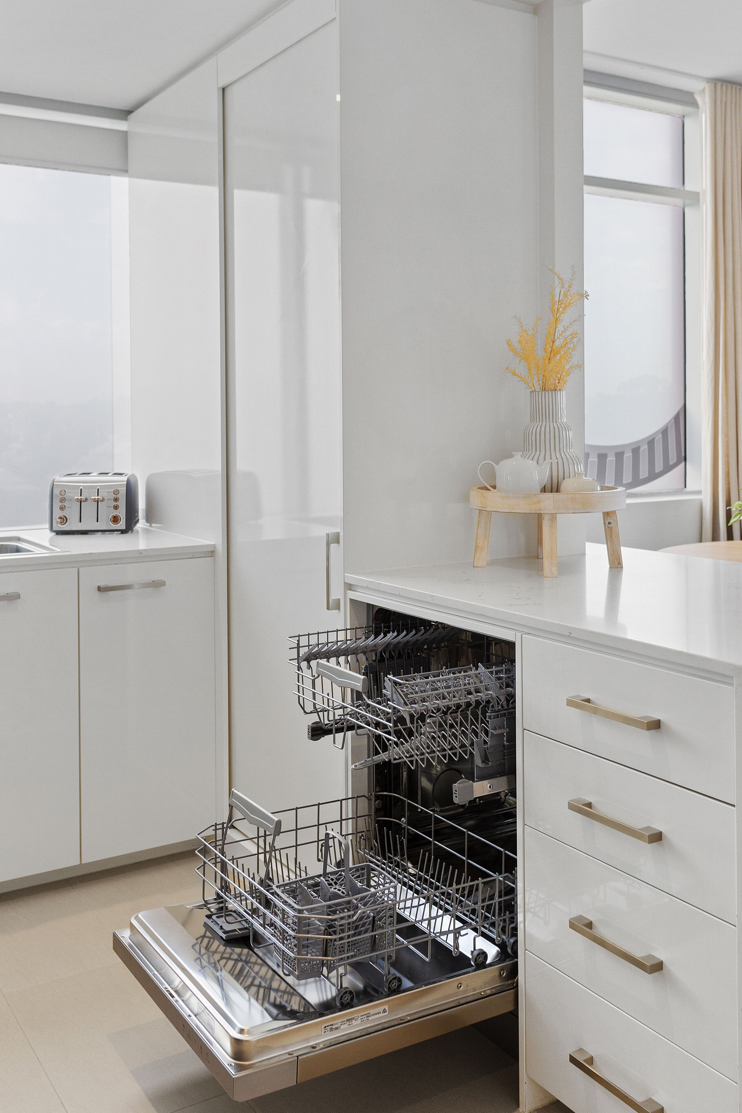 Una cocina moderna con armarios blancos, lavavajillas y tostadora sobre la encimera.