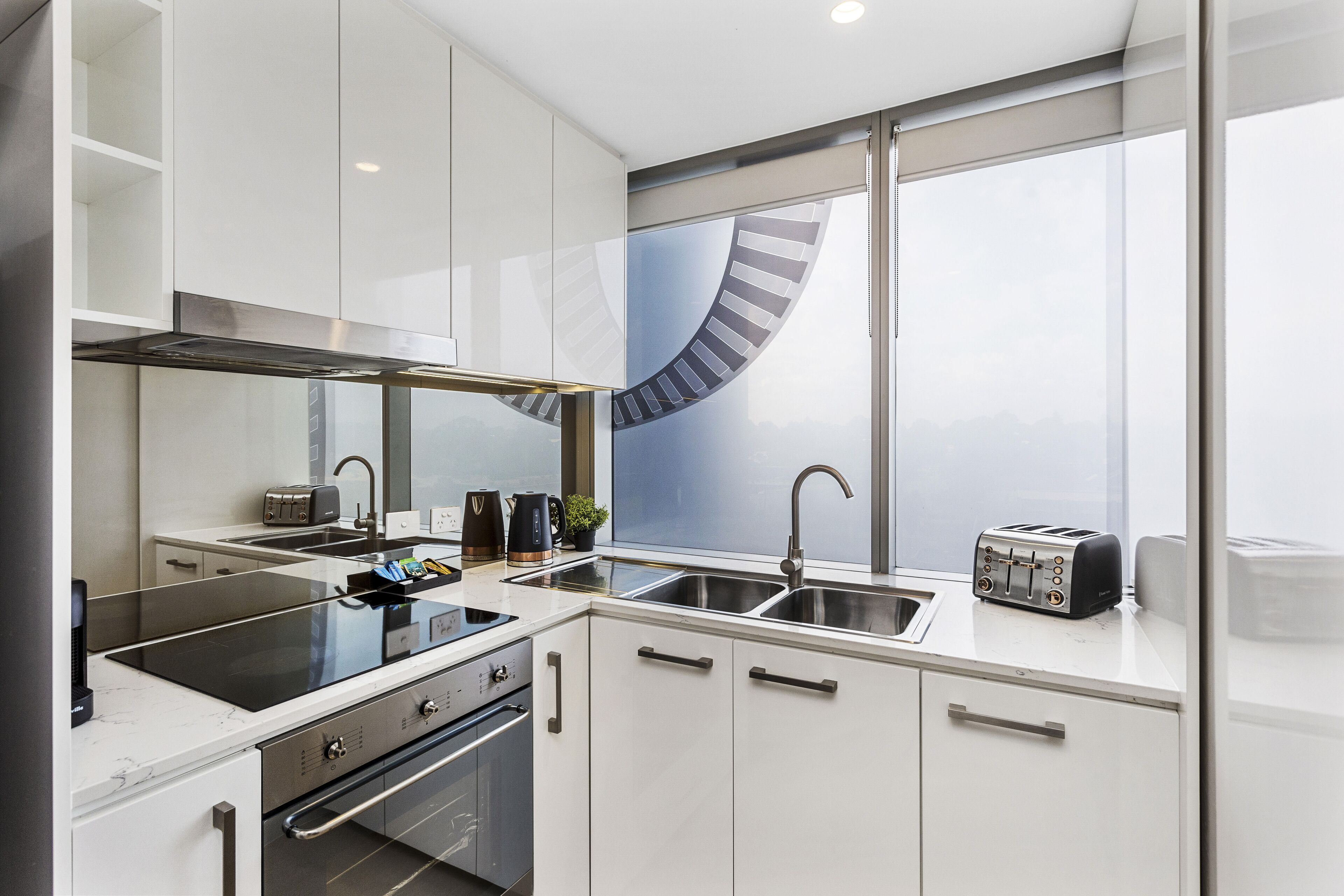 A modern kitchen with white cabinets, a black stove, a sink, and a toaster.