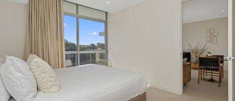 A bedroom with a large bed, a desk, and a view of the outdoors.