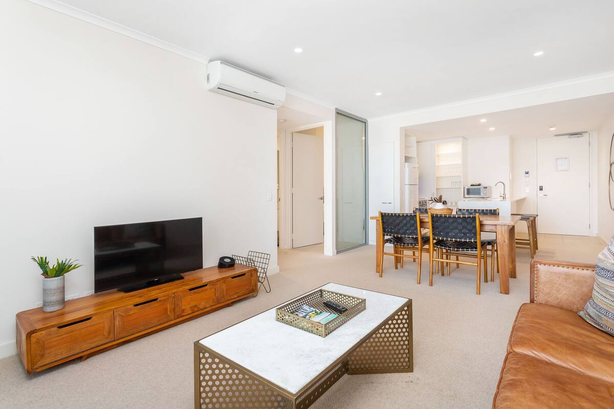 A modern living room with a flat-screen TV, wooden entertainment unit, and a coffee table.