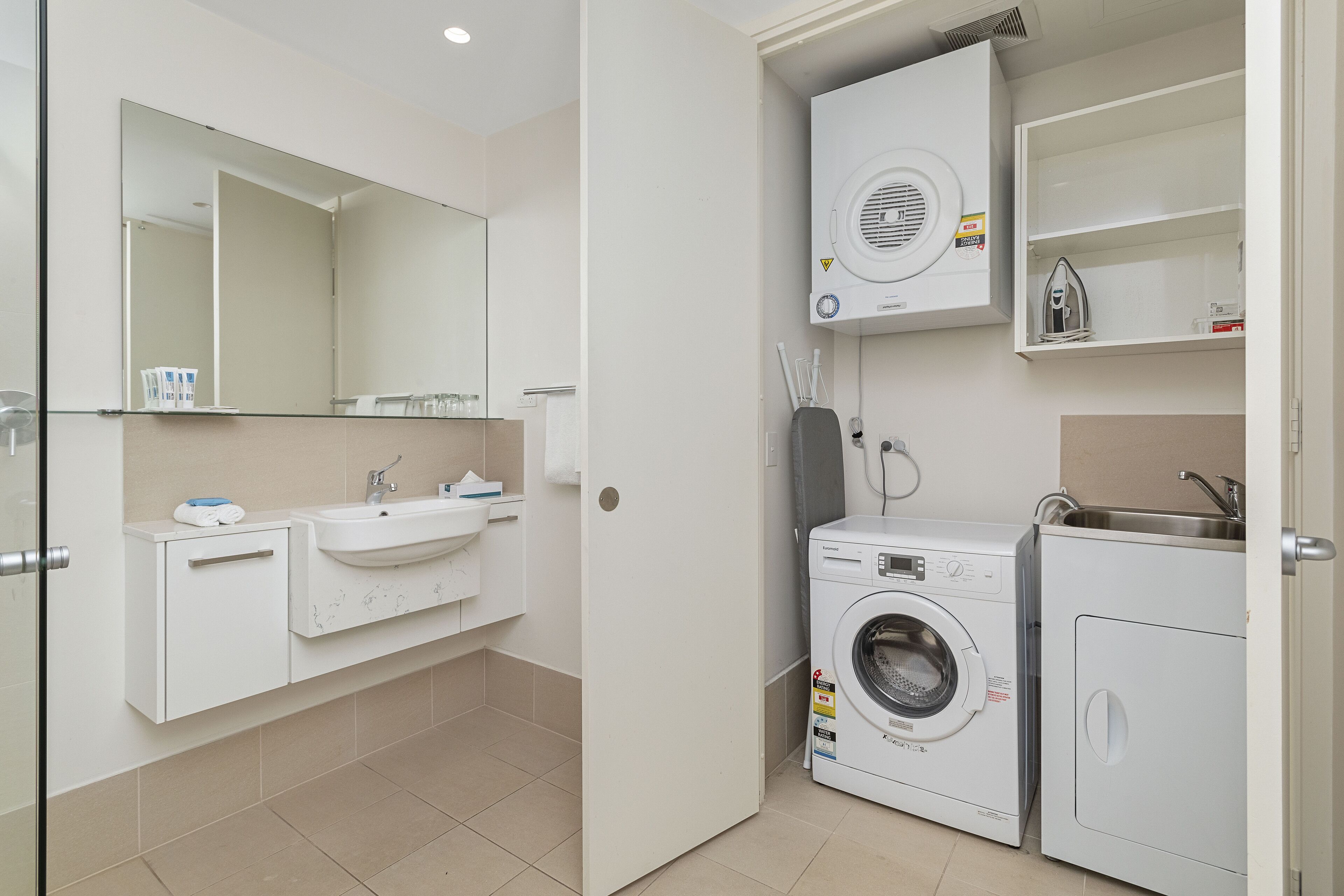 A modern bathroom with a sink, mirror, and a washing machine.