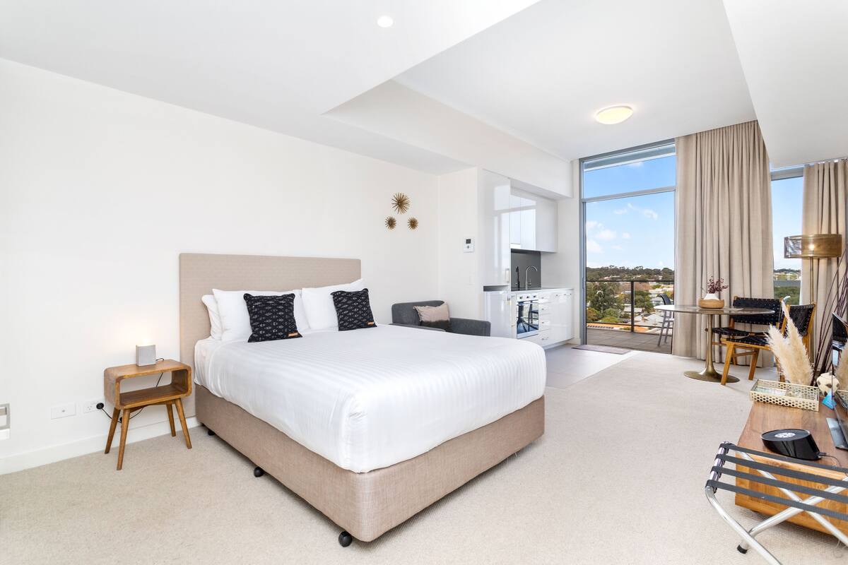 A modern hotel room with a large bed, a desk, and a view of the city.