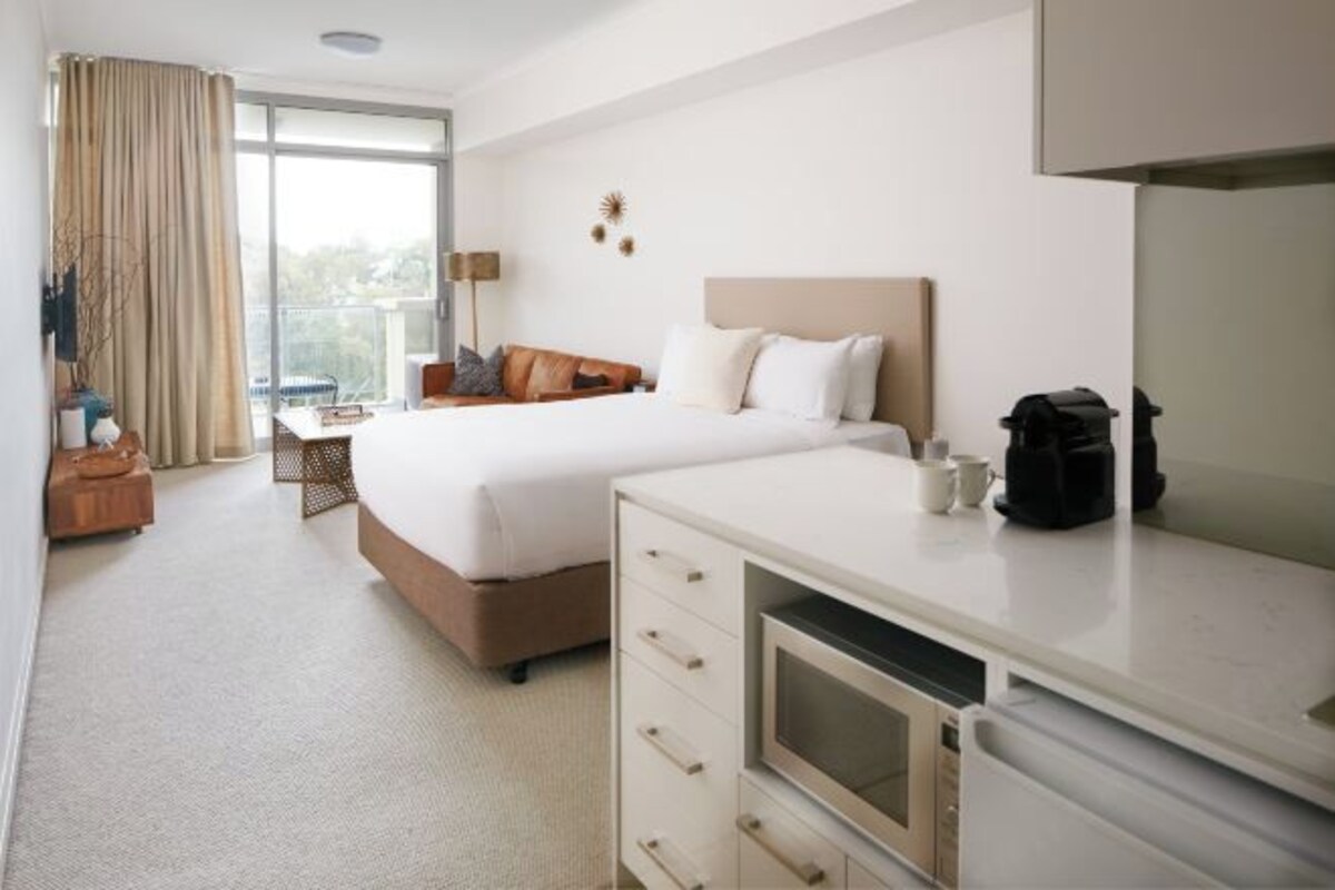 Una habitación de hotel con una cama grande, un escritorio con una silla, un televisor y una kitchenette.