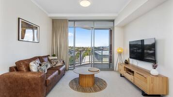 A modern living room with a leather sofa, a round coffee table, a wooden TV stand, and a large window offering a city view.