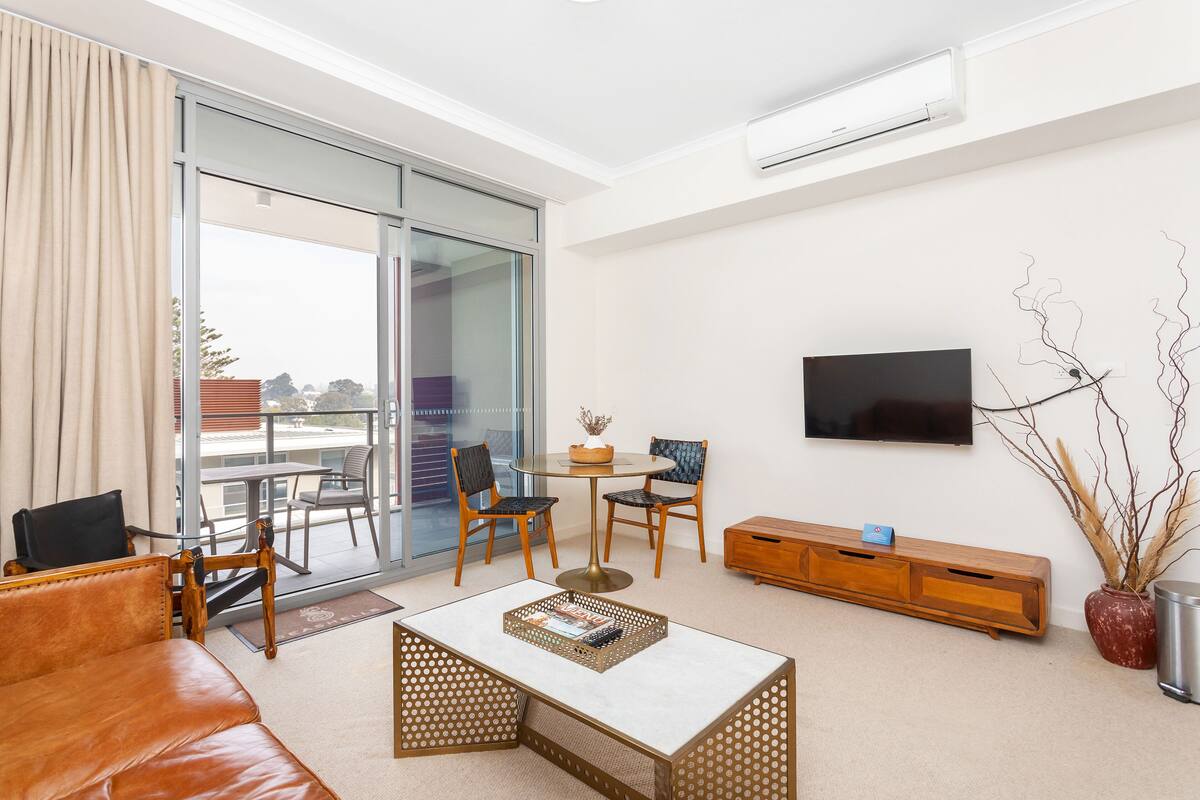 A modern living room with a sofa, coffee table, TV, and a balcony with a table and chairs.