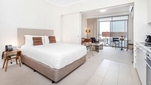 A hotel room with a large bed, a desk, a chair, a dining table, and a kitchenette. - Nautica Residences Fremantle (East Fremantle)