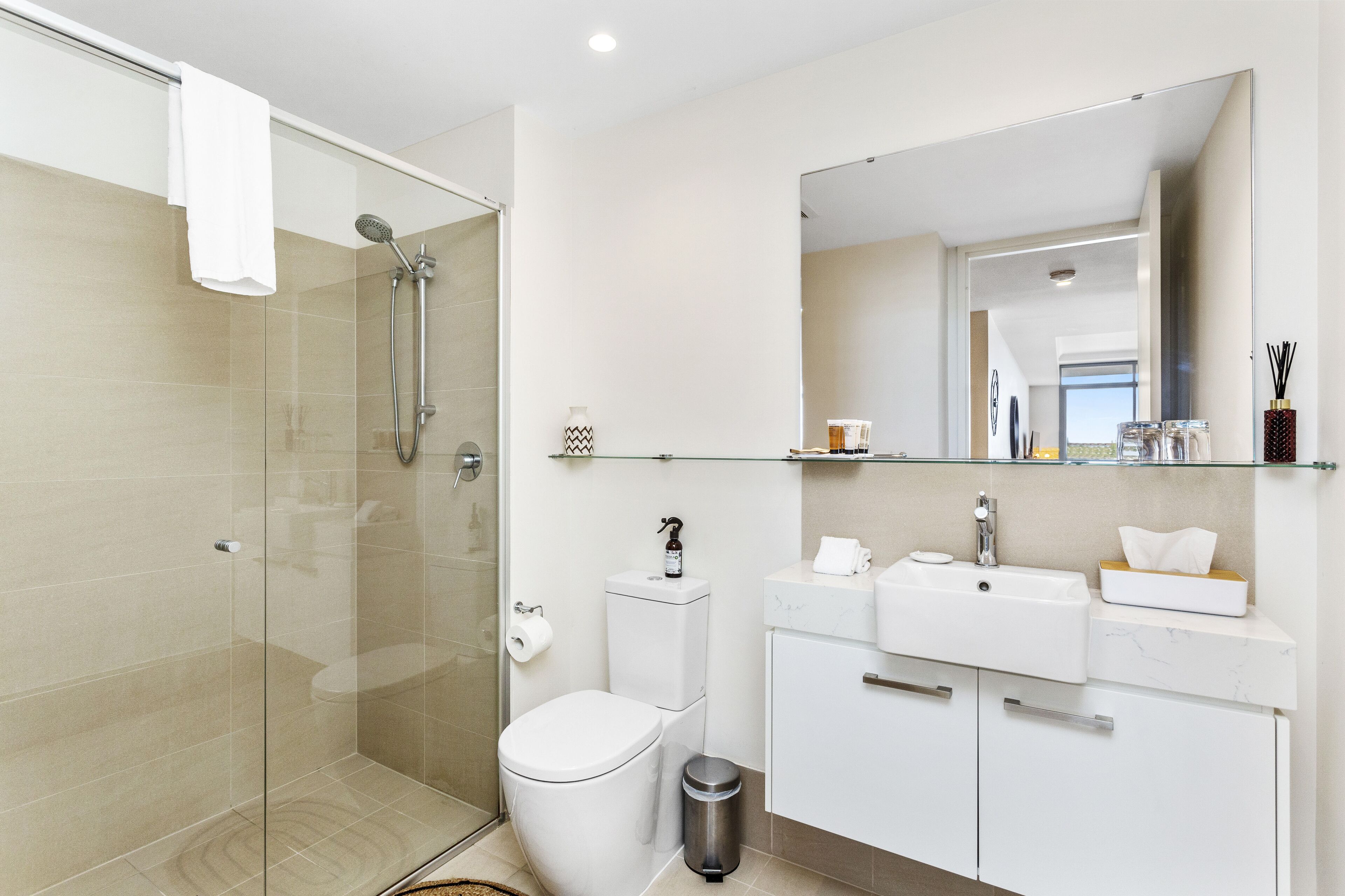 Un baño moderno con cabina de ducha de vidrio, inodoro, lavabo y tocador con espejo.