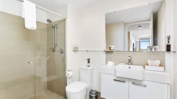 Un baño moderno con cabina de ducha de vidrio, inodoro, lavabo y tocador con espejo.