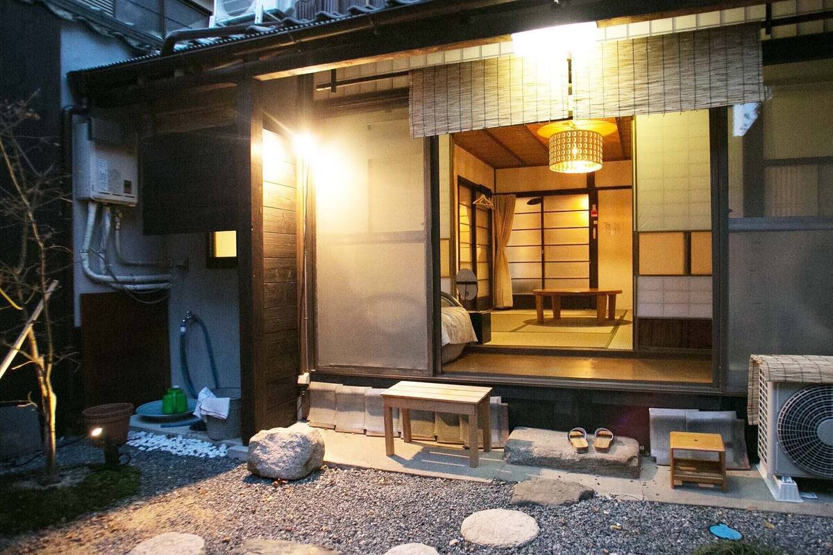 A traditional Japanese ryokan with tatami mat flooring, a wooden exterior, and a sliding door leading to a room with a futon bed.
