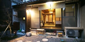 A traditional Japanese ryokan with tatami mat flooring, a wooden exterior, and a sliding door leading to a room with a futon bed. - Guesthouse Hana Nishijin (Kyoto)
