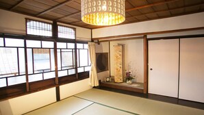 A traditional Japanese room with tatami flooring, sliding doors, and a hanging light fixture. - Guesthouse Hana Nishijin (Kyoto)