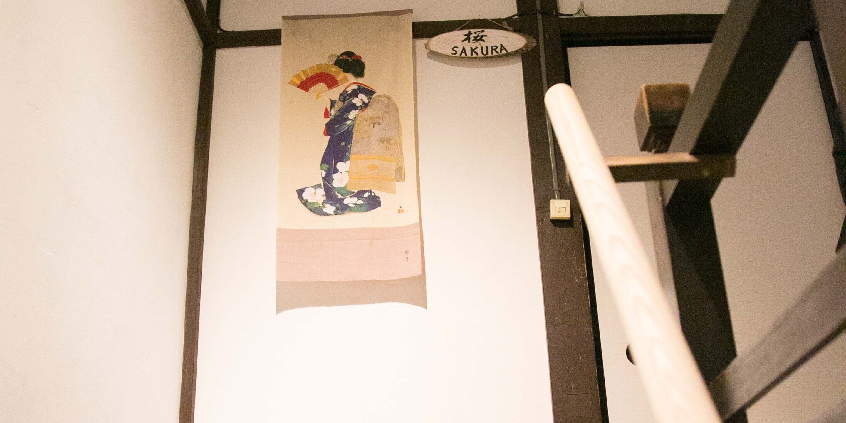 A traditional Japanese artwork hanging on a wall, a sign reading "SAKURA", and a staircase with a handrail.