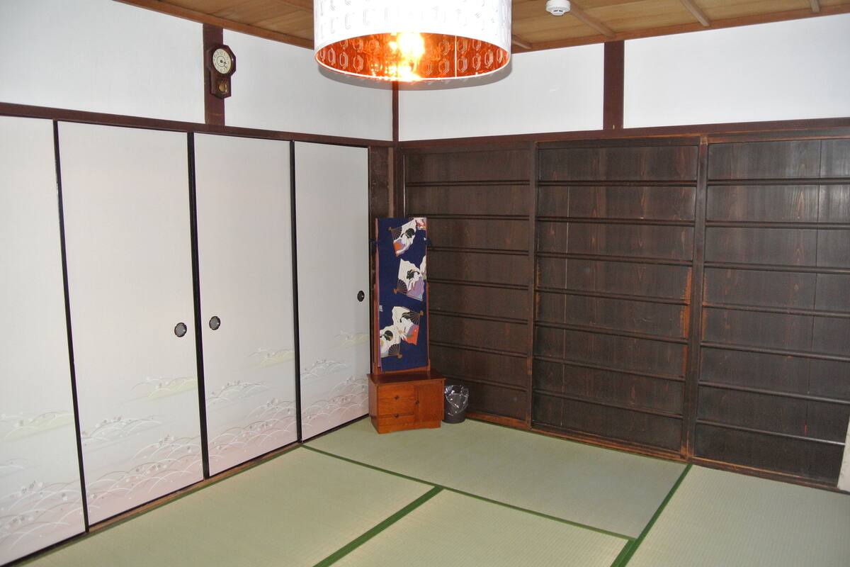 A traditional Japanese room with tatami flooring, sliding doors, and a hanging artwork.