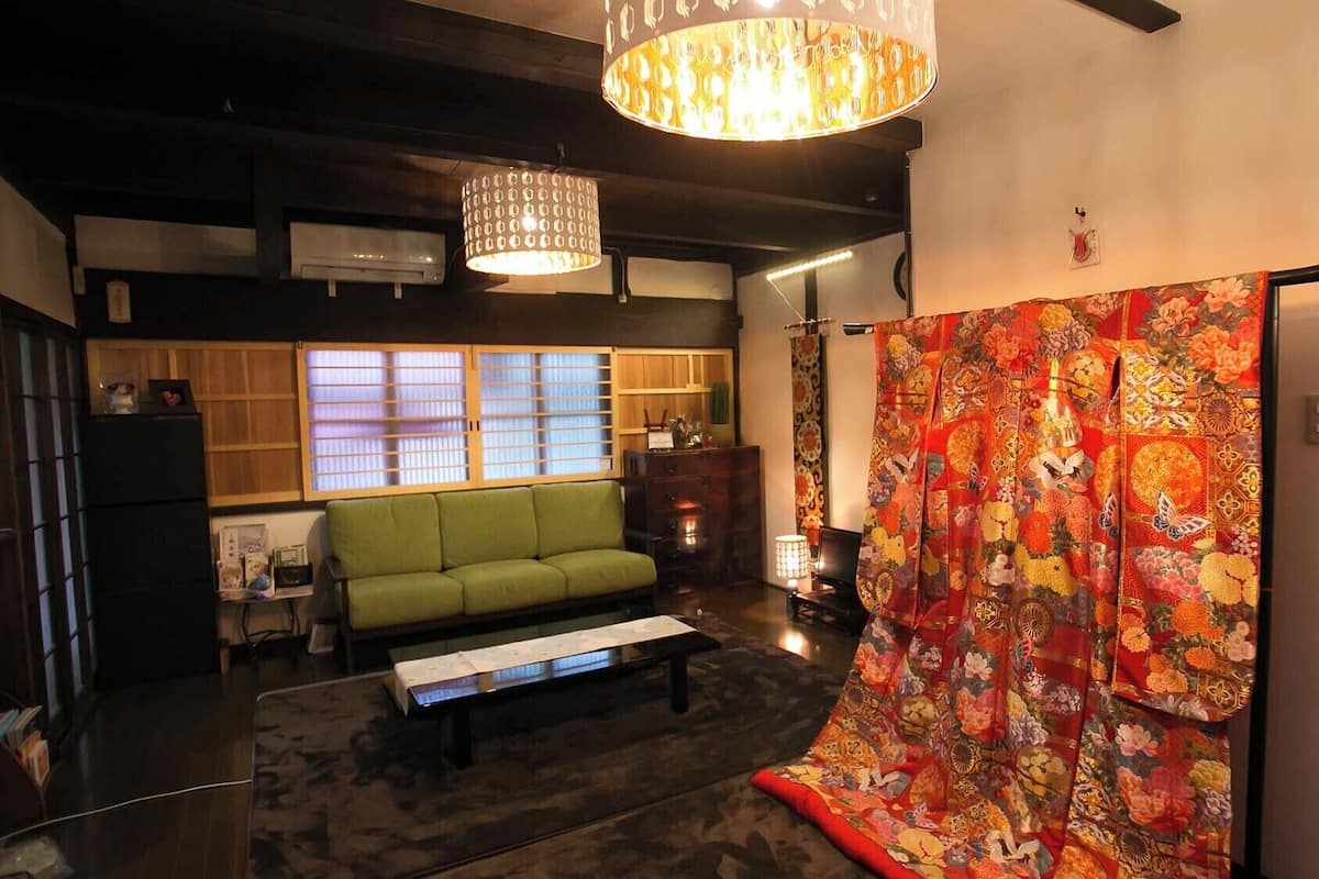 A traditional Japanese room with tatami flooring, a green sofa, a low table, and a colorful shoji screen.