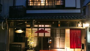 A traditional Japanese house with a wooden exterior, a red awning, and a small garden area with a bamboo plant. - Guesthouse Hana Nishijin (Kyoto)