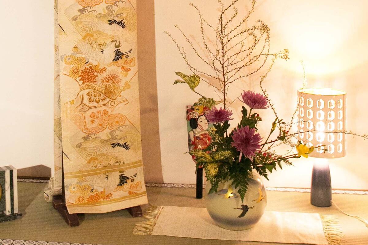 A room with a clock, a decorative curtain, a vase with flowers, and a lamp.
