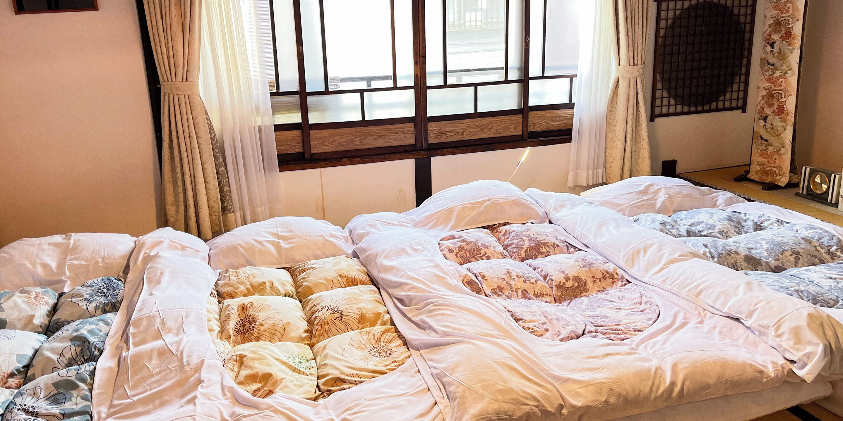 A hotel room with a large bed, a window with wooden frames, and a curtain.