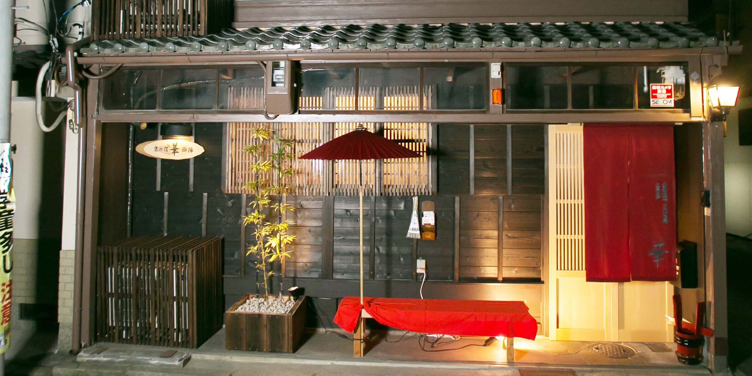Un restaurante japonés tradicional con fachada de madera, una planta de bambú y un paraguas rojo.