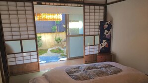 A traditional Japanese-style room with tatami flooring, a futon bed, sliding doors leading to a garden, and a shoji screen. - Guesthouse Hana Nishijin (Kyoto)