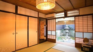A traditional Japanese room with tatami flooring, sliding doors, and a view of a garden. - Guesthouse Hana Nishijin (Kyoto)