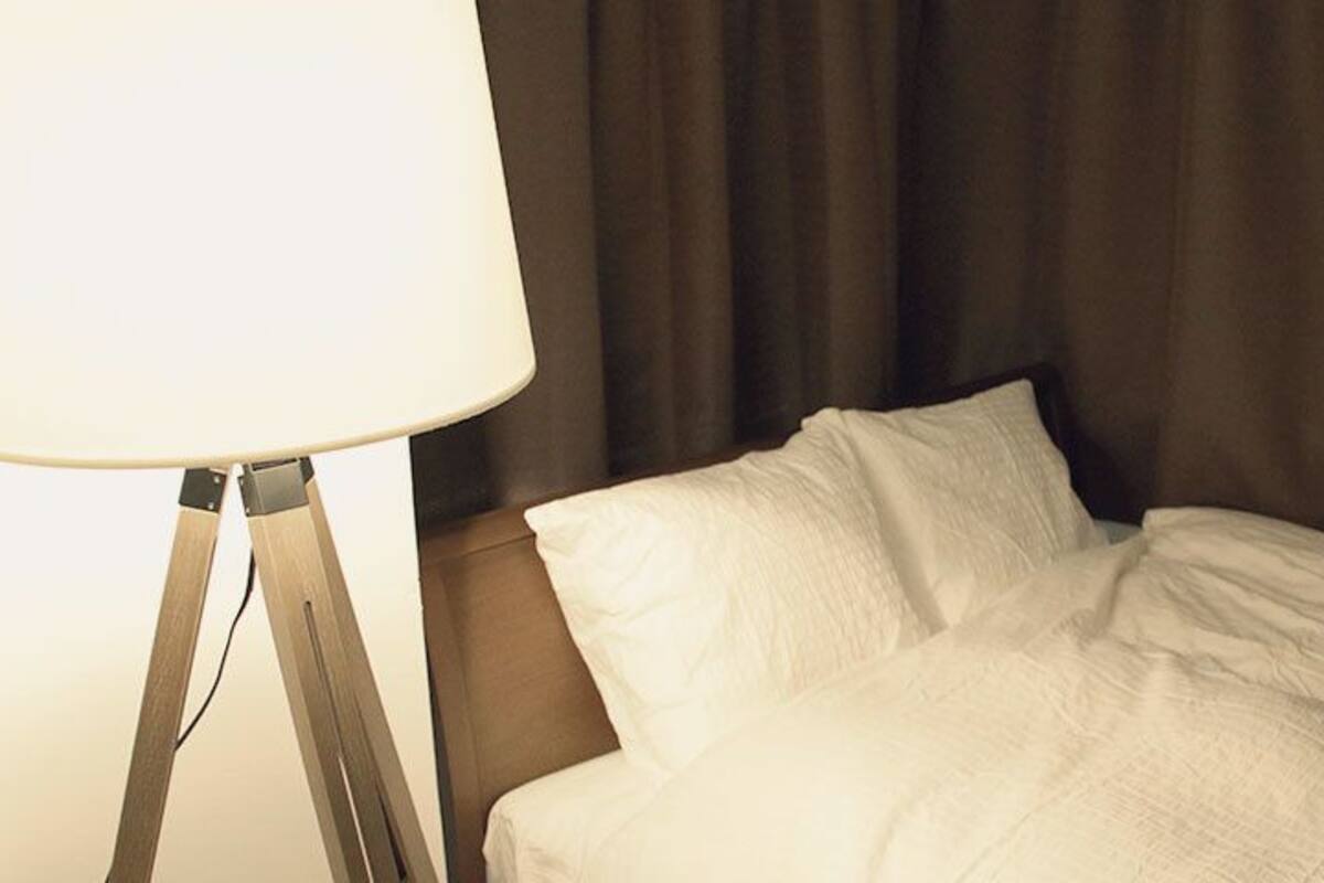 A hotel room with a bed, white bedding, and a lamp on a wooden stand.