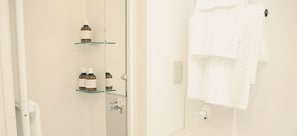 A bathroom with a glass shelf holding toiletries, a towel rack with folded towels, and a visible shower control. - Minato Hotel (Kyoto)