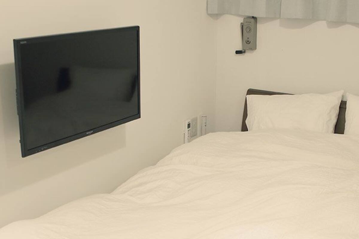 A hotel room with a bed, a flat-screen TV mounted on the wall, and a thermostat on the wall.