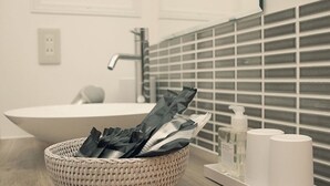 Un baño con un lavamanos blanco, una cesta tejida con artículos de aseo, un dispensador de jabón y un perchero para toallas.