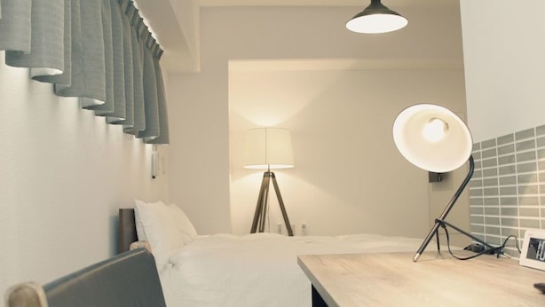 Habitación de hotel con cama, mesita de noche, lámpara y un perchero en la pared.