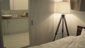 Habitación de hotel con cama, lámpara de noche, mesita de noche y vista al baño.