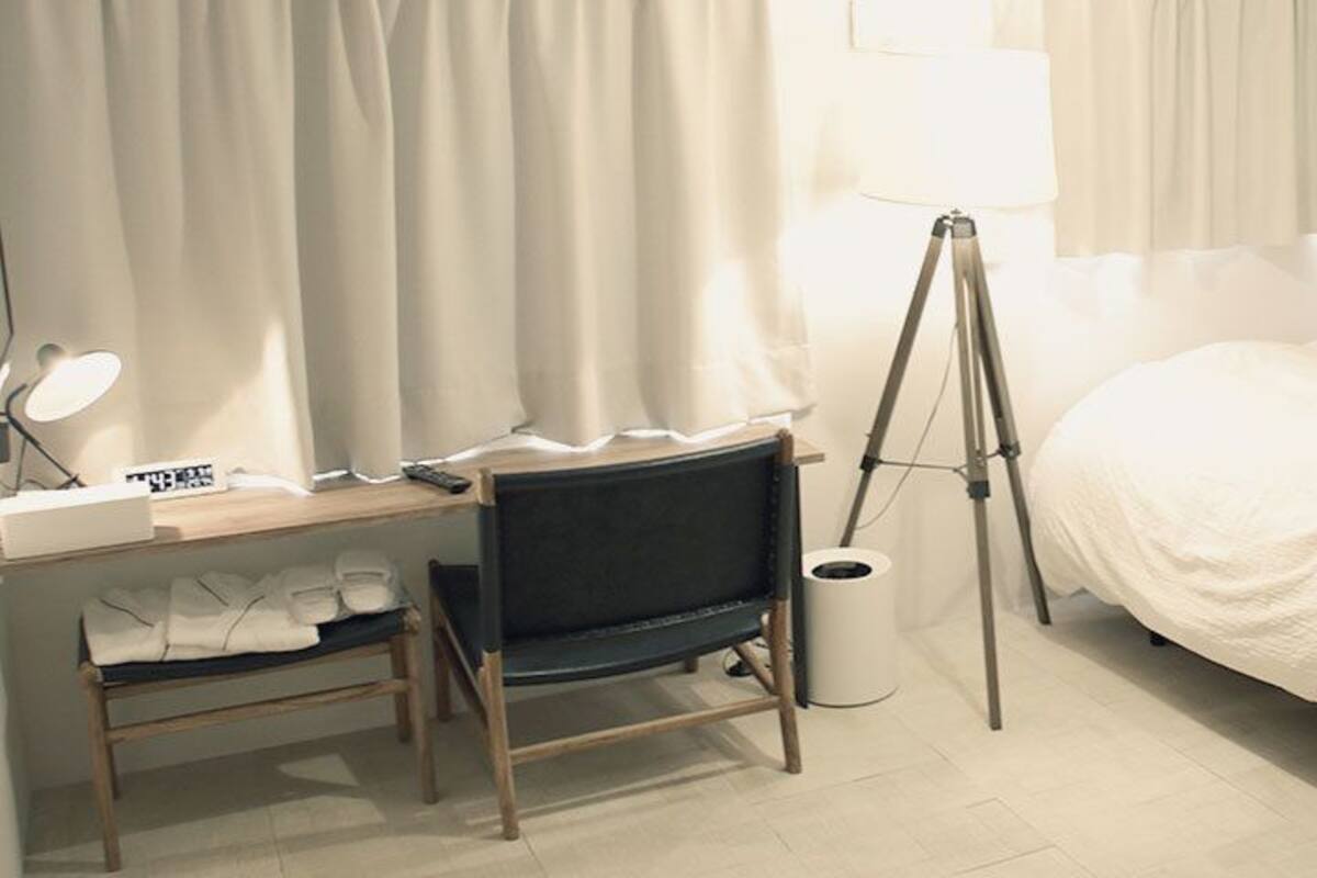 A hotel room with a bed, a desk with a chair, a lamp, and a trash bin.