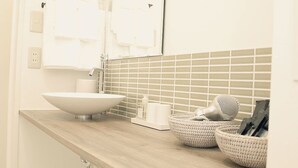 Un baño con lavamanos blanco, un espejo y un salpicadero de azulejos. Hay dos cestas tejidas sobre la encimera.