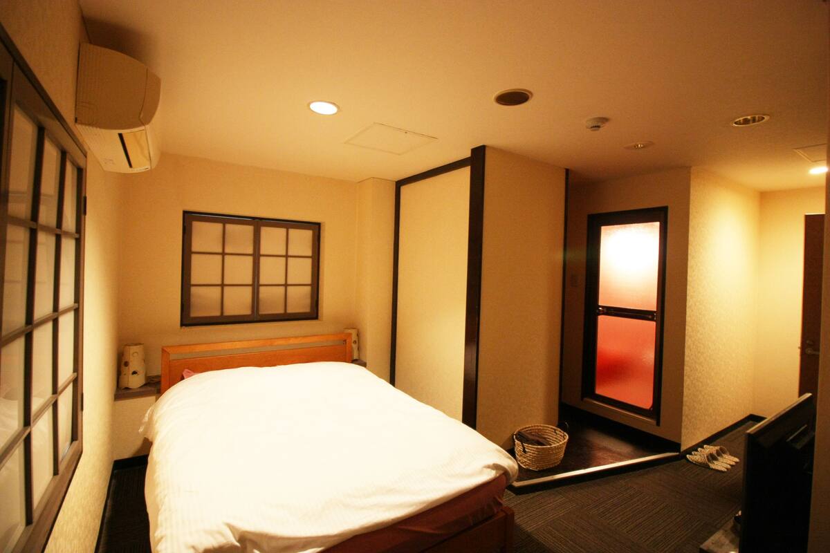 A hotel room with a bed, a television, a window, and a wall-mounted air conditioner.