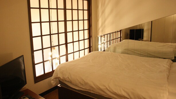 Una habitación de hotel con un ventanal grande, una cama y un televisor sobre un mueble.