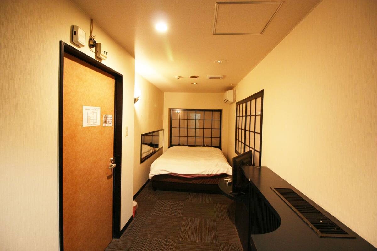 A hotel room with a bed, a desk, a chair, a window, and a door.