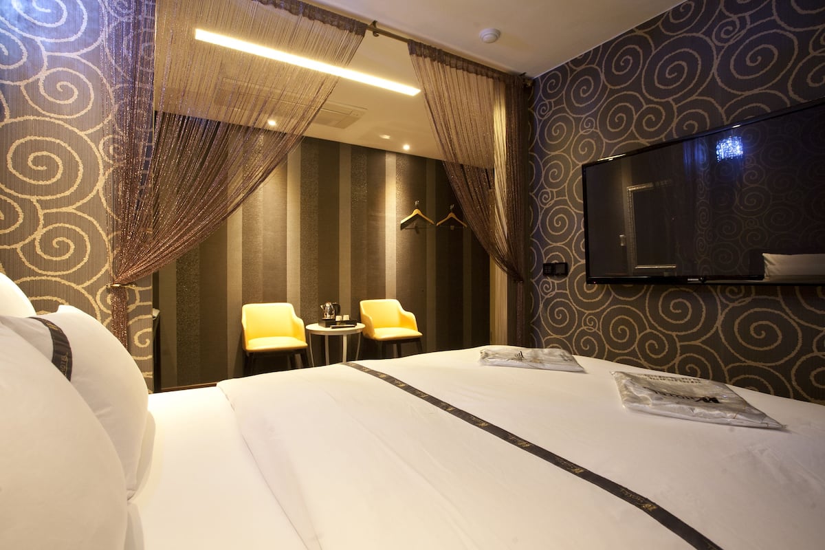 A hotel room with a large bed, two chairs, a small table, and a TV mounted on the wall.
