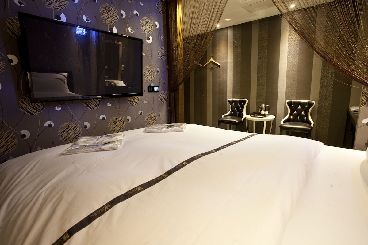 A hotel room with a large bed, a flat-screen TV mounted on the wall, two chairs, and a small table.