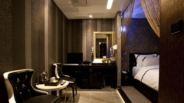 A hotel room with a bed, a desk with a chair, a small table, a mirror, and a nightstand with a lamp. - W Hotel (Incheon)