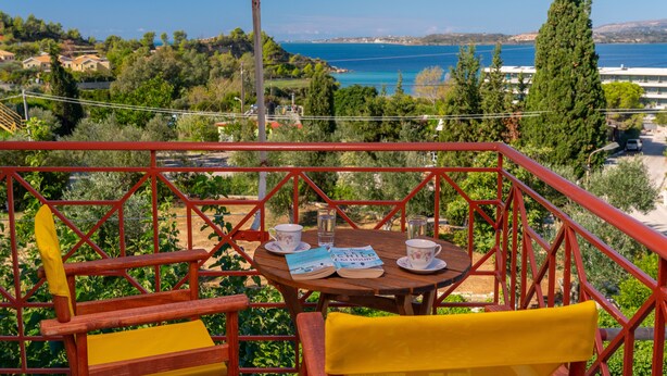 A terrace with a table set for two, overlooking a scenic coastal landscape. - Lorenzo House Apartments (Kefalonia)
